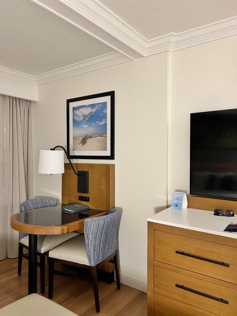 a small table and two chairs with a framed picture on the wall with a small section showing the flatscreen TV in Jupiter Beach Resort King Room