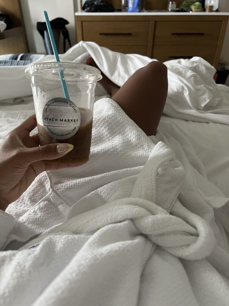 girl laying down in bed wearing a robe holding an iced coffee that says 