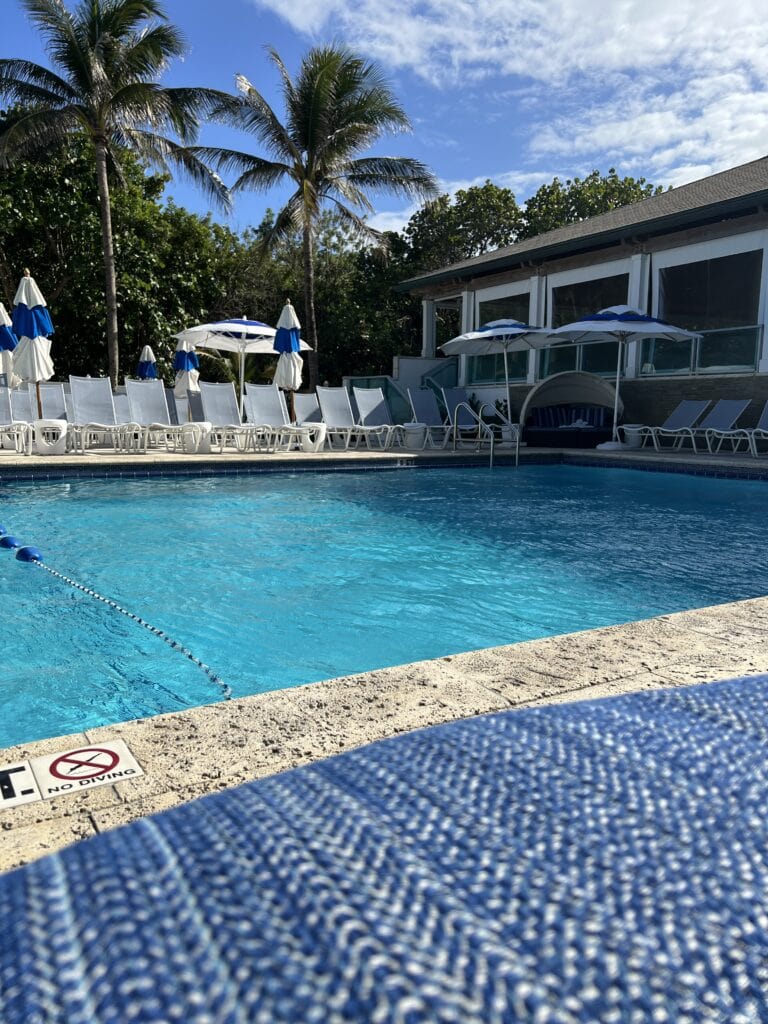 Inviting swimming pool at Jupiter Beach Resort and Spa, flanked by white lounge chairs and vibrant greenery, ideal for a sunny day retreat